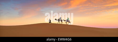 Les touristes en randonnée chamelière au coucher du soleil, désert Erg Chebbi près de Merzouga, Sahara, Maroc Banque D'Images