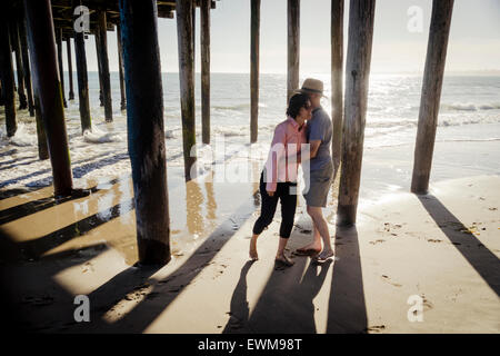 L'homme et de la femme d'âge moyen de désinvolture hugging après la poursuite de l'autre en vertu de la demande à la plage de Piers Banque D'Images