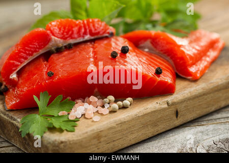 Close up shot avant de cuivre rouge rivière fraîche filets de saumon sur une planche à découper, sel de mer et herbes. Banque D'Images