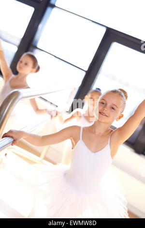 Pretty smiling young ballerina en formation à l'aide de la barre dans l'école de ballet studio de pratiquer ses positions et de l'équilibre avec Banque D'Images