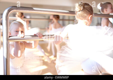 Peu de blanc ballerines faisant un exercice s'étendant à l'aide d'un ballet barre horizontale dans le studio de danse. Banque D'Images