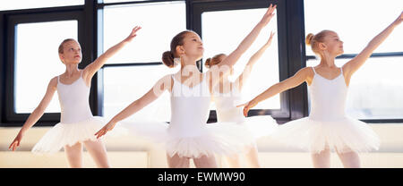 Les jeunes ballerines pratiquant une danse chorégraphiée de pluie toutes leurs armes dans l'unisson gracieux au cours de la pratique à une école de ballet Banque D'Images