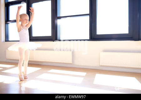 Petite fille formation pour être une ballerine debout dans un bras gracieux position relevée dans son tutu blanc et satin rose chaussures de ballet Banque D'Images