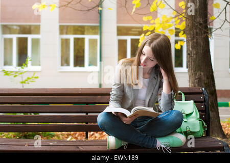 Student sitting on bench and reading book Banque D'Images