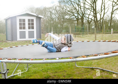 Un heureux garçon blond assis sur un trampoline dans le jardin Banque D'Images