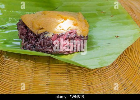 Le riz gluant noir avec de la crème anglaise, enveloppés dans des feuilles de bananier Banque D'Images