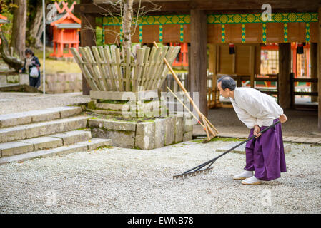 Un prêtre shintoïste ratisse un jardin zen de gravier au Sanctuaire Kasuga-Taisha à Nara, au Japon. Banque D'Images