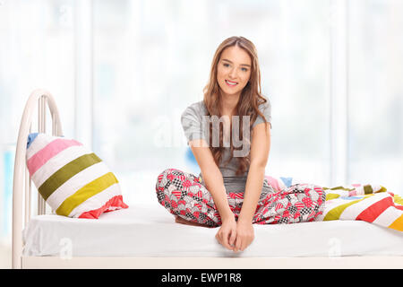 Jeune femme brune en pyjama assis sur un lit et regardant la caméra à la maison Banque D'Images