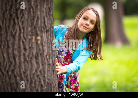 Cute little girl peeking de derrière un arbre. Banque D'Images