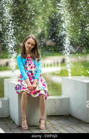 Jolie petite fille assise près de la fontaine. Banque D'Images