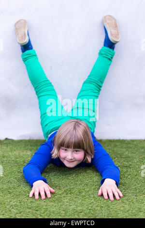 Young caucasian girl lying tête en bas contre le mur sur l'herbe à l'aire de jeux Banque D'Images