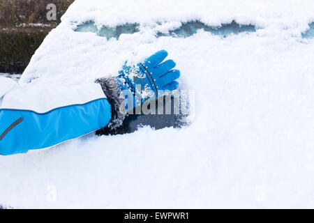 Bras avec gant bleu l'enlèvement de la neige à partir de la fenêtre de voiture en hiver Banque D'Images