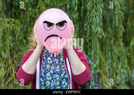 Teenage girl holding balloon with angry face comme expression dans la nature Banque D'Images