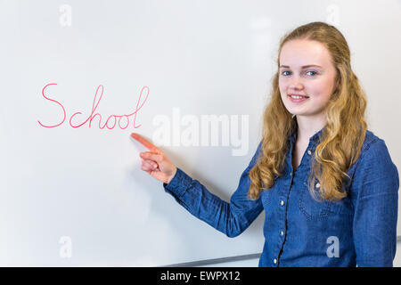 Portrait of teenage girl pointing at École mot écrit sur un tableau blanc dans la classe Banque D'Images