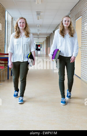 Deux caucasian teenage girls walking in school corridor long texte comptable books Banque D'Images