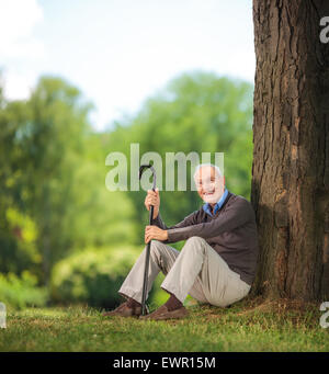 Casual man canne et assis sur l'herbe dans un parc et à la recherche à l'appareil photo avec objectif de décentrement et Banque D'Images