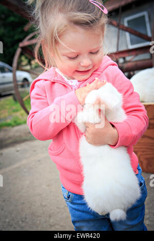 Petite fille avec un lapin en face de la ferme Banque D'Images