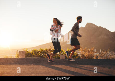 Jeune couple jogging tôt le matin, avec retour à la femme par dessus son épaule. Jeune homme et femme d'exécution à l'extérieur sur un pays Banque D'Images