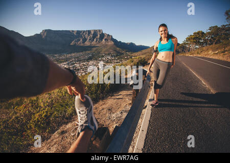 Fit young woman standing avec l'homme étend sa jambe à l'extérieur, sur route de campagne. Les jeunes coureurs se détendre après matin couru. POV sho Banque D'Images