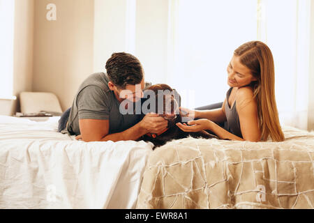 Tiré d'un jeune couple avec leur chien sur le lit le matin. Jeune homme et femme, passer du temps avec leur animal de compagnie dans la chambre. Banque D'Images