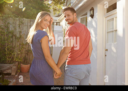 Piscine shot of young caucasian couple walking à leur maison se tenant la main, à la fois regard sur les épaules et en souriant est venu Banque D'Images