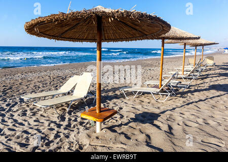 Parasols de plage de paille et chaises longues sur la plage vide de Réthymnon, Crete Beach Grèce Europe Banque D'Images