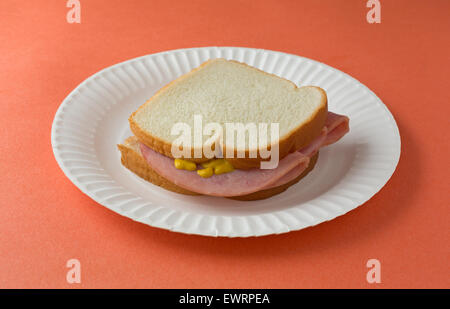 Un sandwich au jambon à la moutarde au miel sur pain blanc sur une assiette en carton et orange de table. Banque D'Images