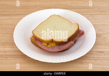 Un sandwich au jambon à la moutarde au miel sur pain blanc sur une assiette en carton et le bois de la table. Banque D'Images