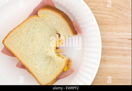 Vue de dessus d'un sandwich au jambon au miel avec de la moutarde sur le pain blanc qui a été mordue sur une assiette en carton et le bois de la table. Banque D'Images