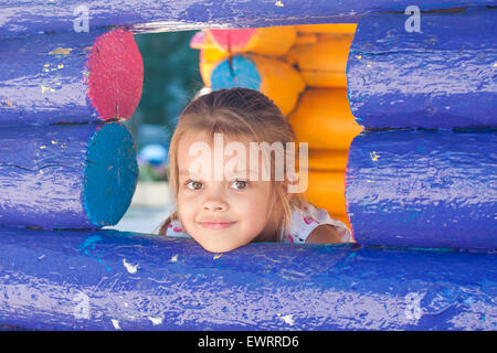 Fille de cinq ans jouant sur l'aire de jeux a l'air à partir d'une fenêtre en bois Banque D'Images