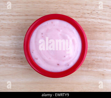 Vue de dessus d'une petite portion de yogourt aux fraises crème dans un bol rouge en haut d'une table en bois éclairé par la lumière de la fenêtre. Banque D'Images