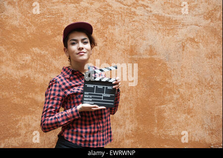 Jeune femme en chemise rouge et le chapeau avec movie clapper board derrière orange wall Banque D'Images