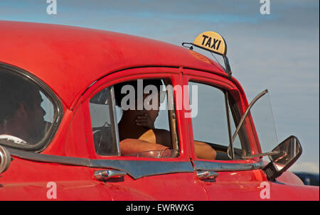 La Havane, Cuba, 12/2010. La femme et l'homme en attente à l'intérieur d'une vieille voiture américaine rouge classique des années 50, utilisé comme un taxi. Banque D'Images