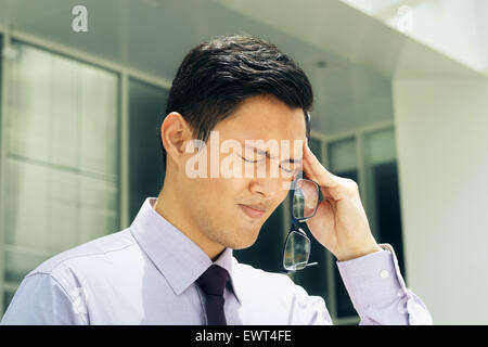 Portrait of asian businessman avec vue problème, se frottant avec l'expression de la douleur du temple. L'homme se trouve dans une rue à l'off Banque D'Images