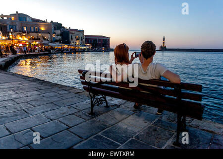 Personnes sur un banc Chania port Crète coucher de soleil Grèce été Banque D'Images