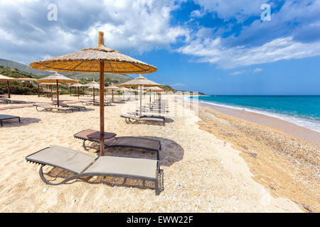 Parasols en lignes pour l'ombre sur la plage de sable à l'autre avec la mer bleue en Grèce Banque D'Images