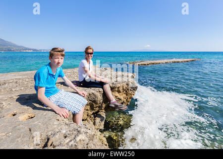 La mère et le fils en tant que touristes assis sur la roche du blue sea profitant de locations Banque D'Images