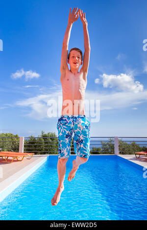 Teenage boy jumping européen haut au-dessus de piscine bleu Banque D'Images