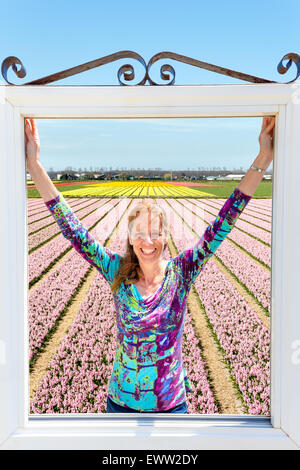 Happy caucasian middle aged woman standing in fenêtre à champ de fleurs roses en Hollande Banque D'Images