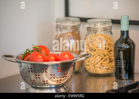 Passoire contenant des tomates bien mûres, une bouteille d'huile d'olive, et un pot de rotinis sur un comptoir de cuisine en acier inoxydable Banque D'Images