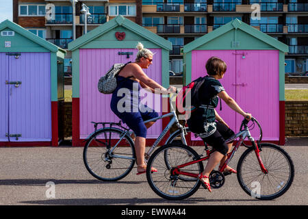 Des promenades cyclistes passé cabines colorées sur le front de mer de Brighton, Brighton, Sussex, UK Banque D'Images