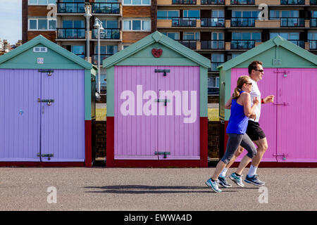 Un couple Jogg passé cabines colorées sur le front de mer de Brighton, Brighton, Sussex, UK Banque D'Images