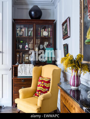 Fauteuil wingback jaune en face de noyer display cabinet in salon lambrissé Banque D'Images