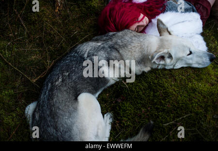 La substance des rêves et cauchemars : Une jeune femme de race blanche aux cheveux rouge seul fille dormir dans une sombre forêt de pins avec un chien-loup blanc comme Banque D'Images