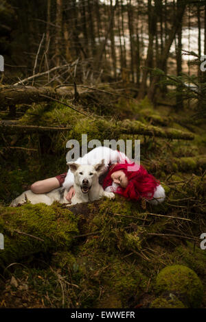 La substance des rêves et cauchemars : Une jeune femme de race blanche aux cheveux rouge seul fille dormir dans une sombre forêt de pins avec un chien-loup blanc comme Banque D'Images