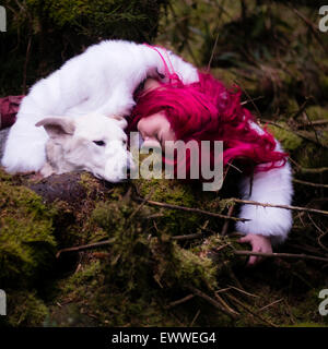 La substance des rêves et cauchemars : Une jeune femme de race blanche aux cheveux rouge seul fille dormir dans une sombre forêt de pins avec un chien-loup blanc comme Banque D'Images