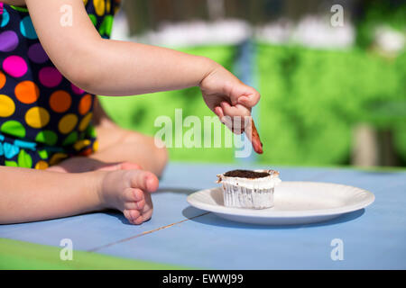 Cute baby wearing spotted dégustation maillot un petit gâteau avec son doigt Banque D'Images