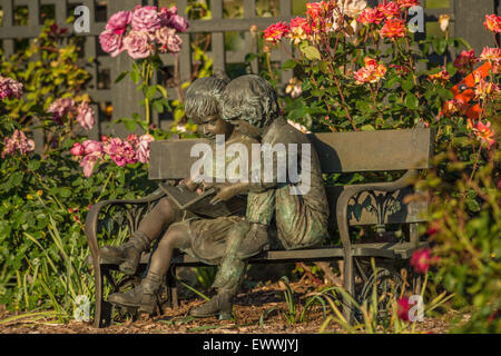 Sculpture Bronze Max Turner d'un garçon et fille lisant sur un banc situé dans un jardin de fleurs Banque D'Images