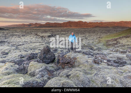 Homme randonnée solitaire sur un champ de lave en Islande, les montagnes en arrière-plan éclairé par le soleil couchant Banque D'Images