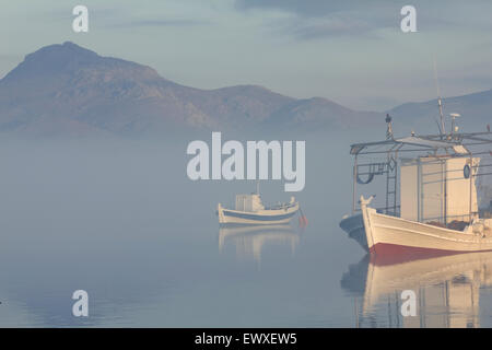 Vue d'un bateau de pêche en bois stern post (premier plan) et un bateau cyan se reflétant dans les paysages aquatiques de Diapori misty bay, Limnos, Banque D'Images